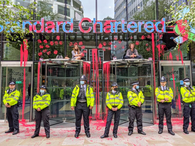 Line of police officers in front of the Standard Chartered covered in fake blood