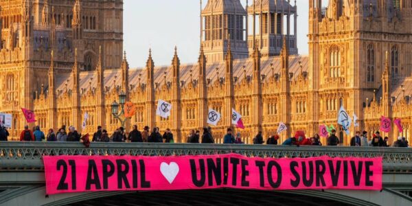 Image of people holding a large banner saying Unite to Survive, with Parliament in the background