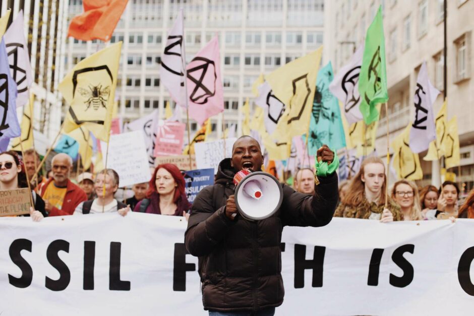Photograph from a march with many extinction banners. A woman with a megaphone stands in front of a long banner.