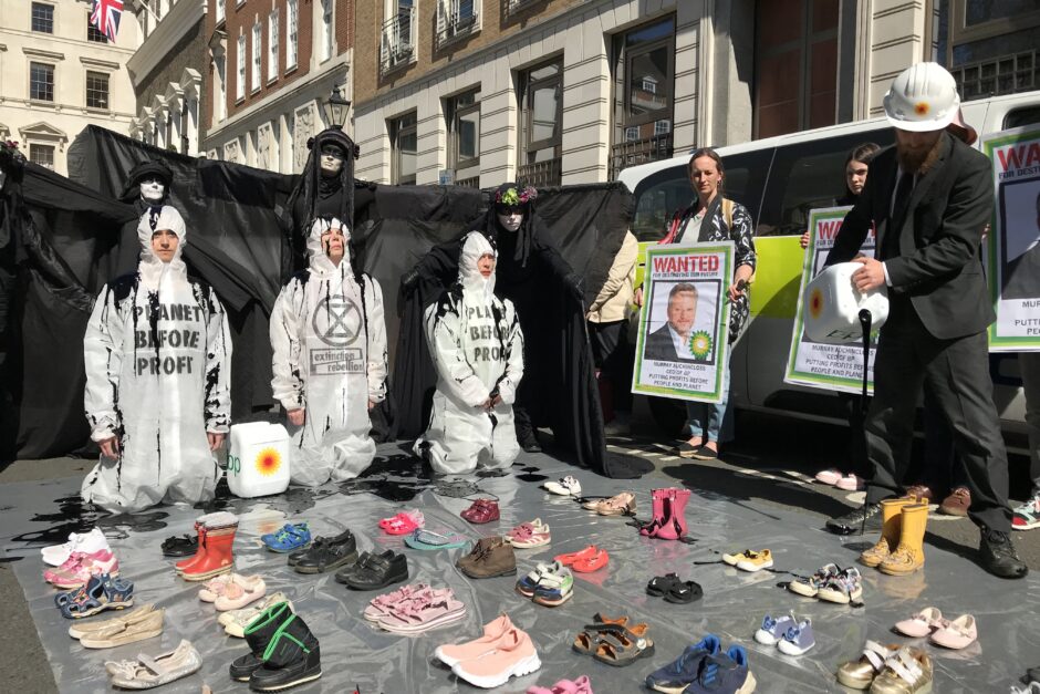 Three Rebels kneel before empty children's shoes while a man dressed in BP-branded uniform pours oil over them.