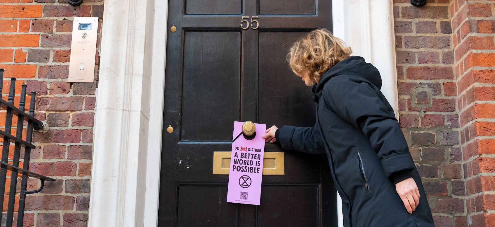 A woman puts an Extinction Rebellion door hanger on a front door knocker